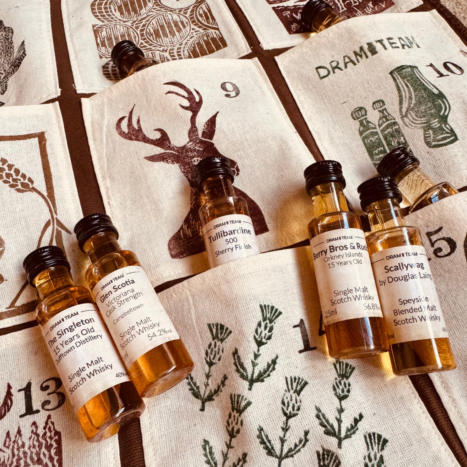 Collection of whisky miniatures on a decorative fabric advent calendar with Scottish-themed designs.