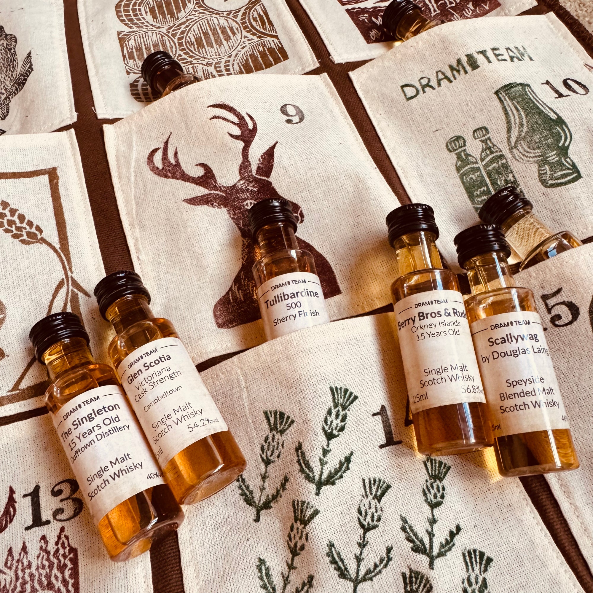 Collection of whisky miniatures on a decorative fabric advent calendar with Scottish-themed designs.
